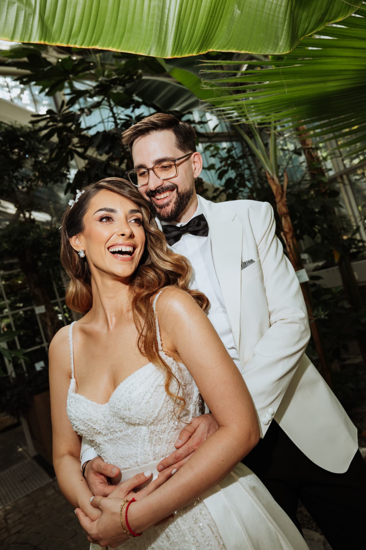 Jelena and Vladimir laughing together beneath tropical leaves on their wedding day, Belgrade, Serbia.