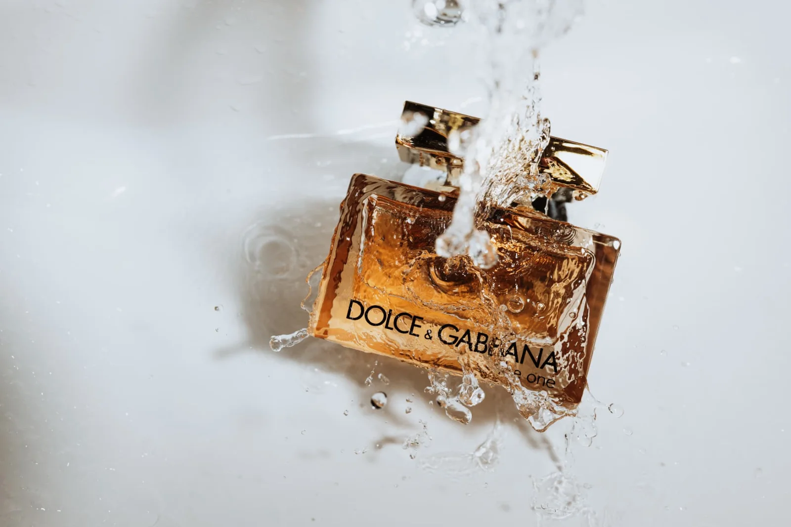 Wedding morning detail: a perfume bottle lying in a white basin as water splashes over it.